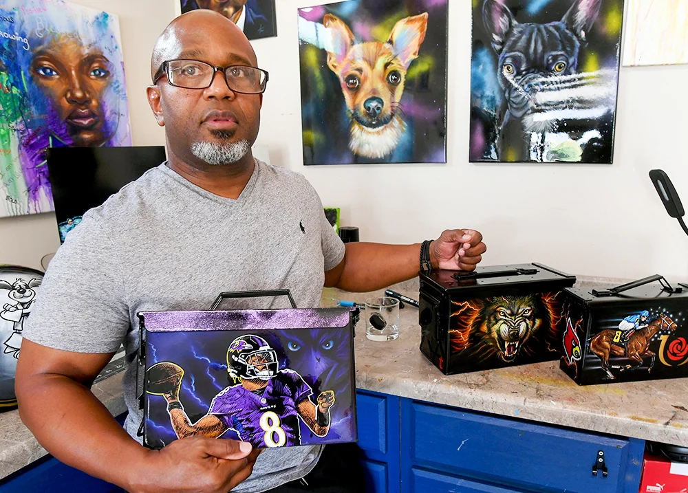 Man holding hand-painted boxes with paintings on the wall behind him