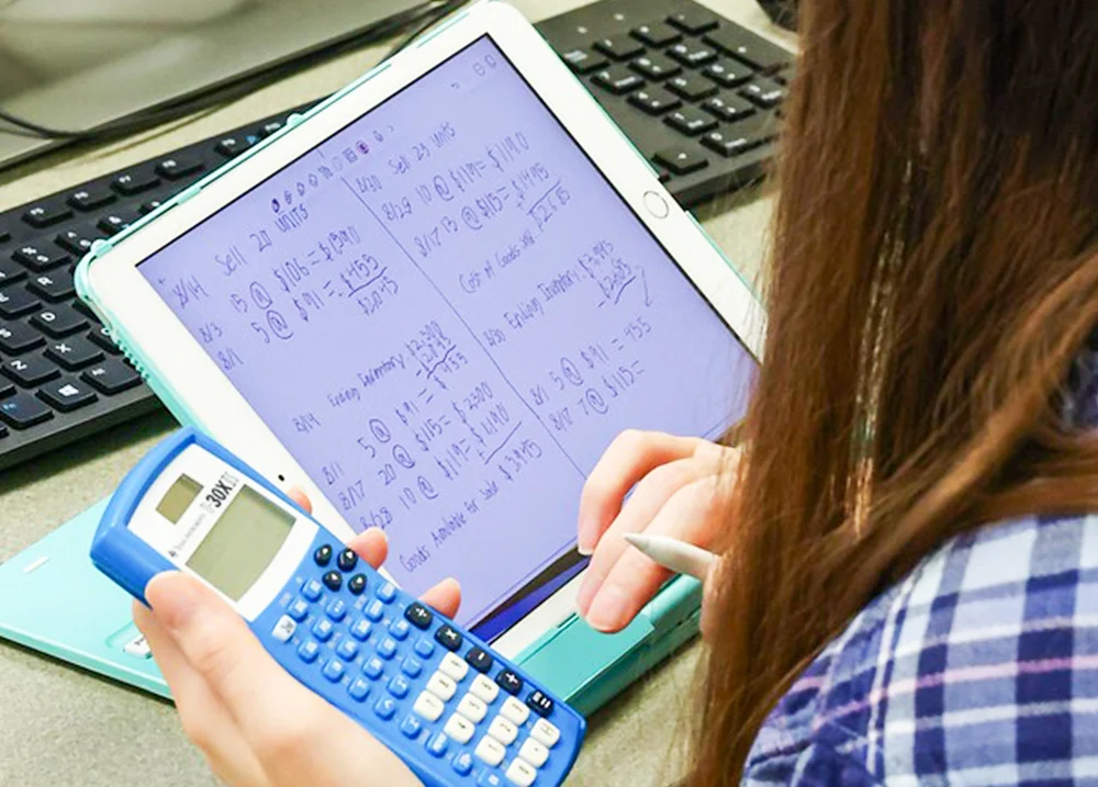 Person doing calculations on a tablet while holding a calculator