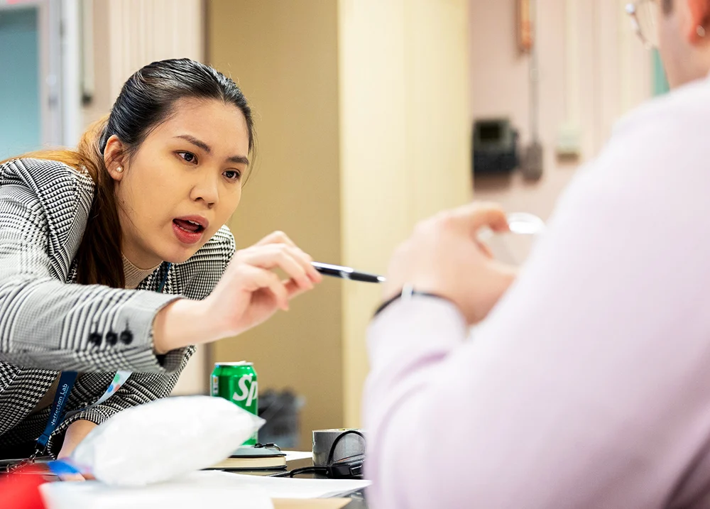 Woman leaning over a table, pointing at something in another person's hand