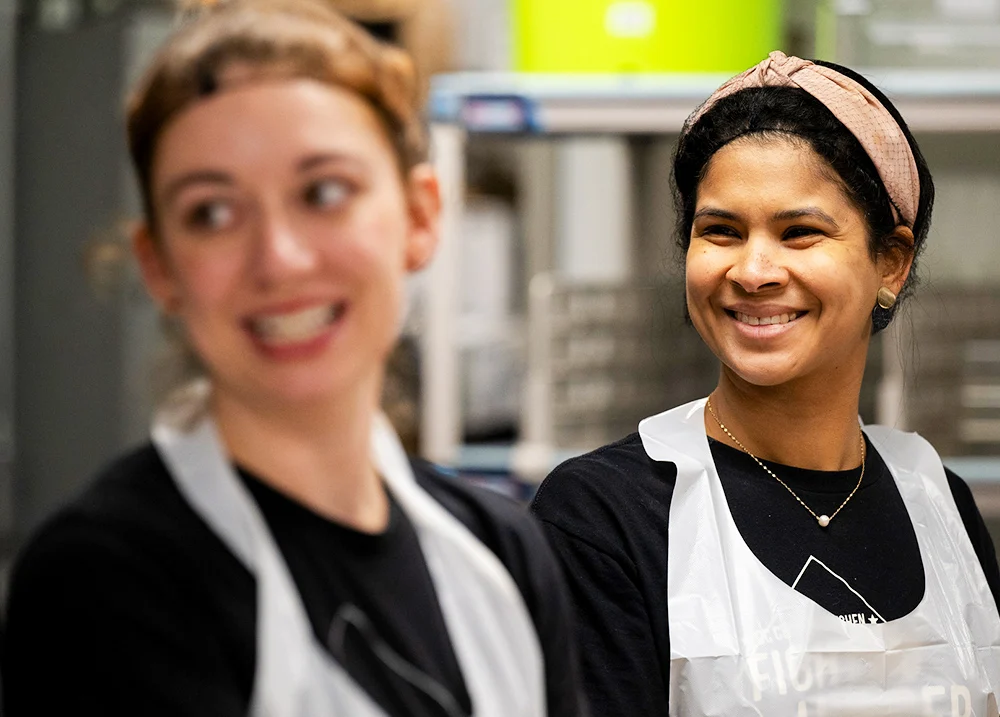Two young women wearing aprons and smiling