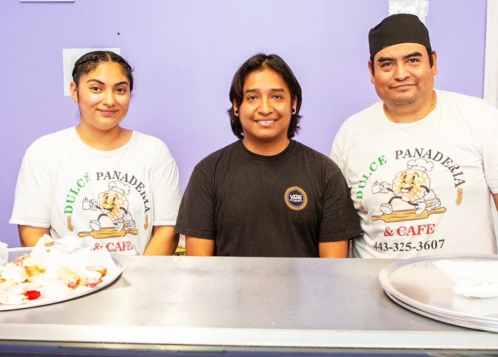 Three people smile and pose for a picture behind a business counter