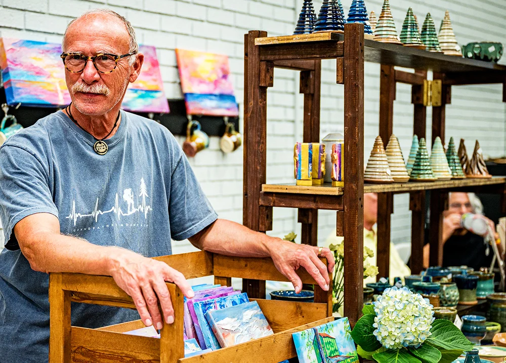 Man at a craft fair leans on a display and looks to the side