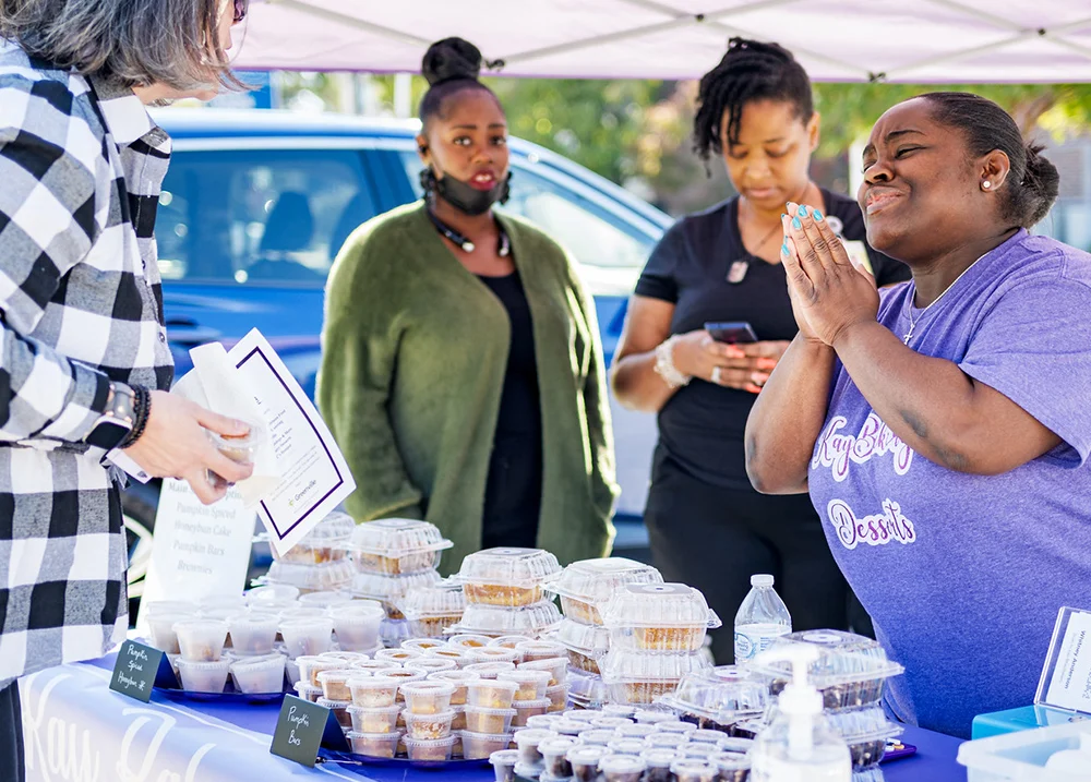 Woman selling something at an outdoor event thanks a customer with two workers standing in the background