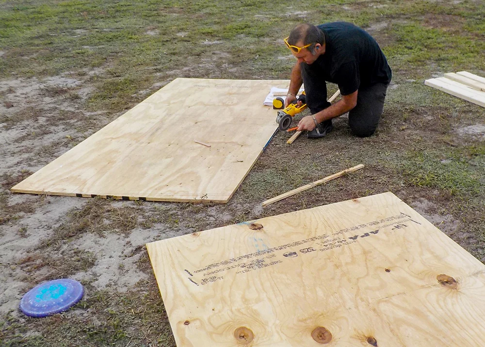 Man kneeling on ground between two large sheets of wood