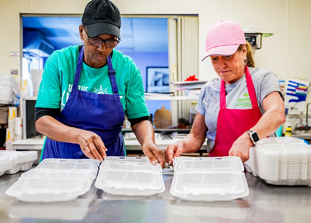 Two people wearing aprons setting out Styrofoam boxes