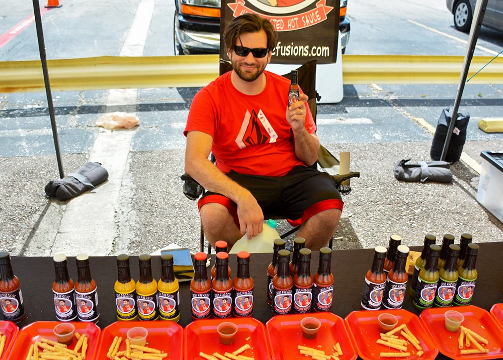Man sitting in a parking lot at a vendor booth selling sauces