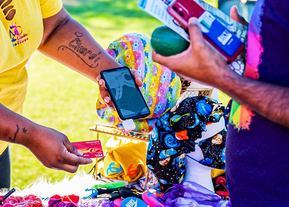A vendor at an outdoor market swipes a credit card through a device that's plugged into their phone