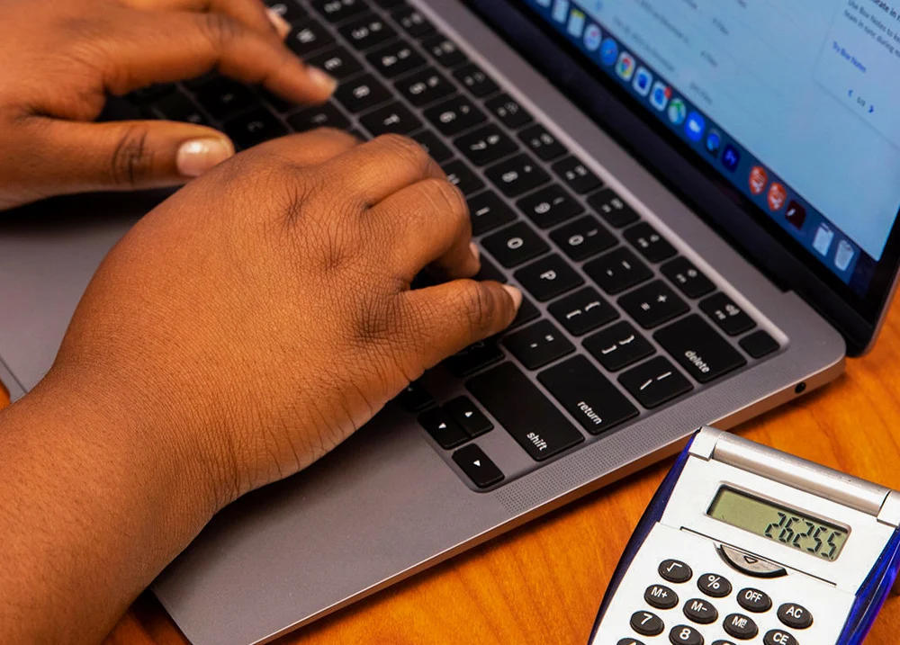 Hands typing on a laptop keyboard that has a calculator next to it