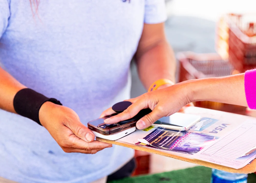 Person holding a clip board with a small payment terminal on it while another person scans their phone across it