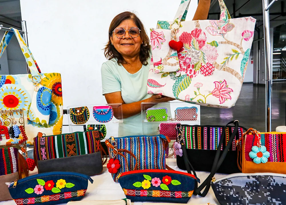 Woman holding a large bag at a vendor table that is selling other purses and bags