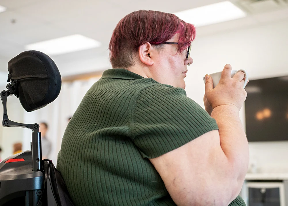 Person who uses a wheelchair holding a coffee and looking forward thinking