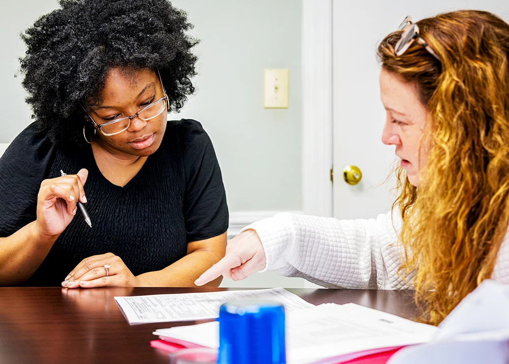 Two women sitting together pointing at something on a piece of paper between them