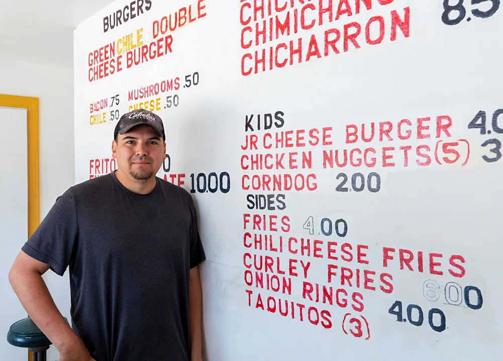 Man stands next to a large menu that's painted on the wall of a restaurant