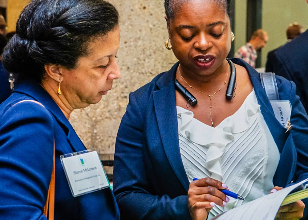 Two women stand next to each other looking at a piece of paper one of them holds