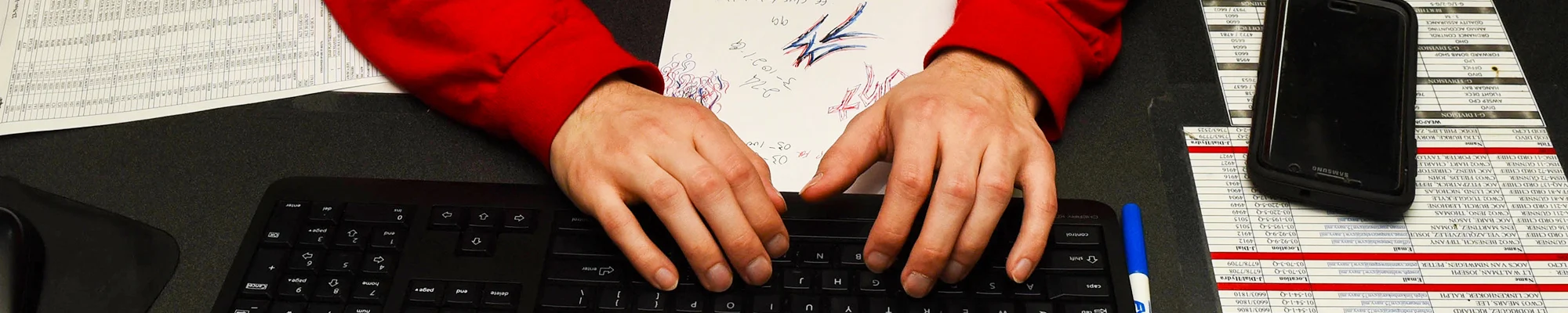 Hands typing on a keyboard with papers and notes scattered about
